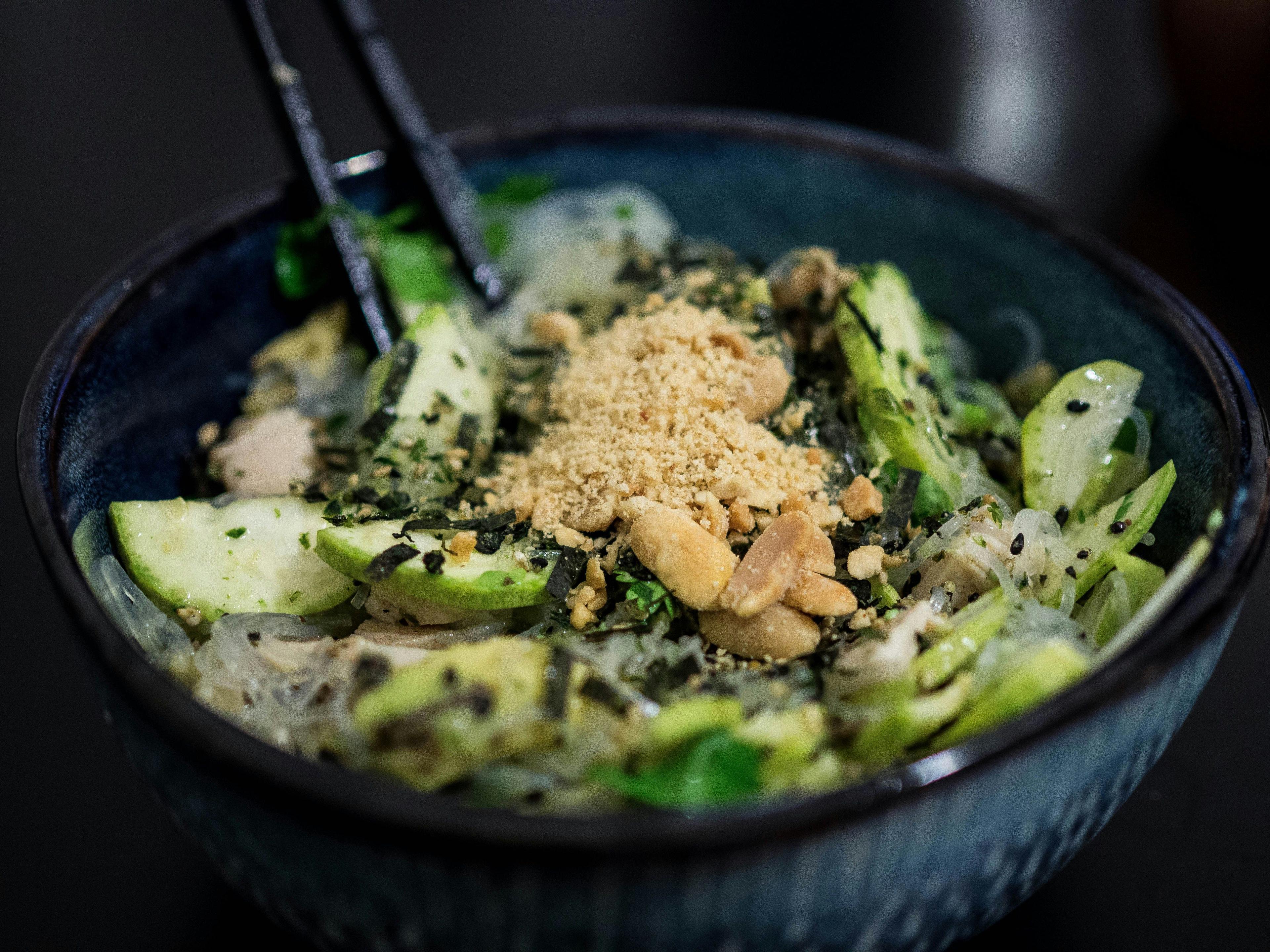 a bowl of food with broccoli, cucumbers, and seasoning