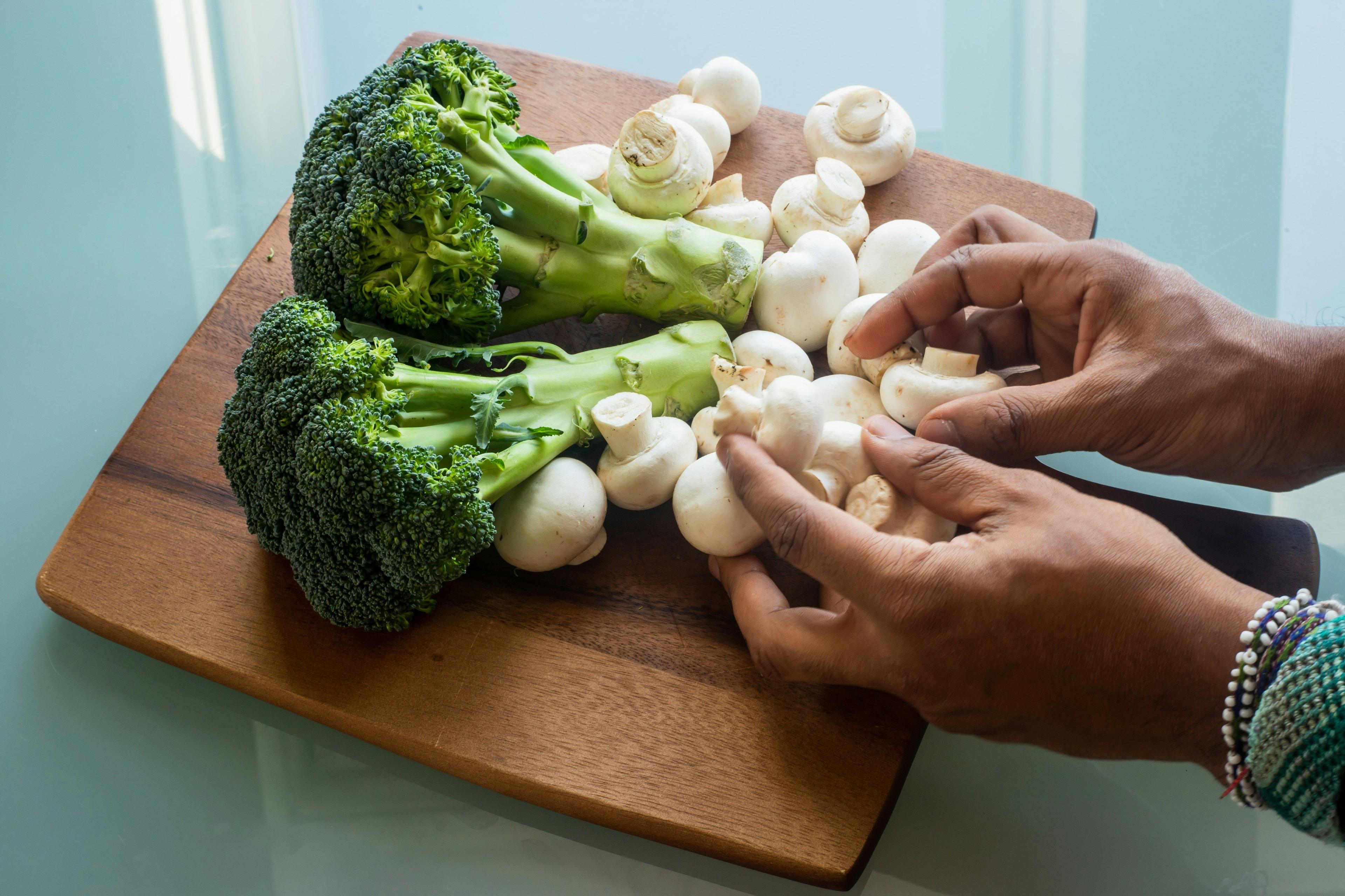 a person cutting up broccoli and mushrooms on a cutting board