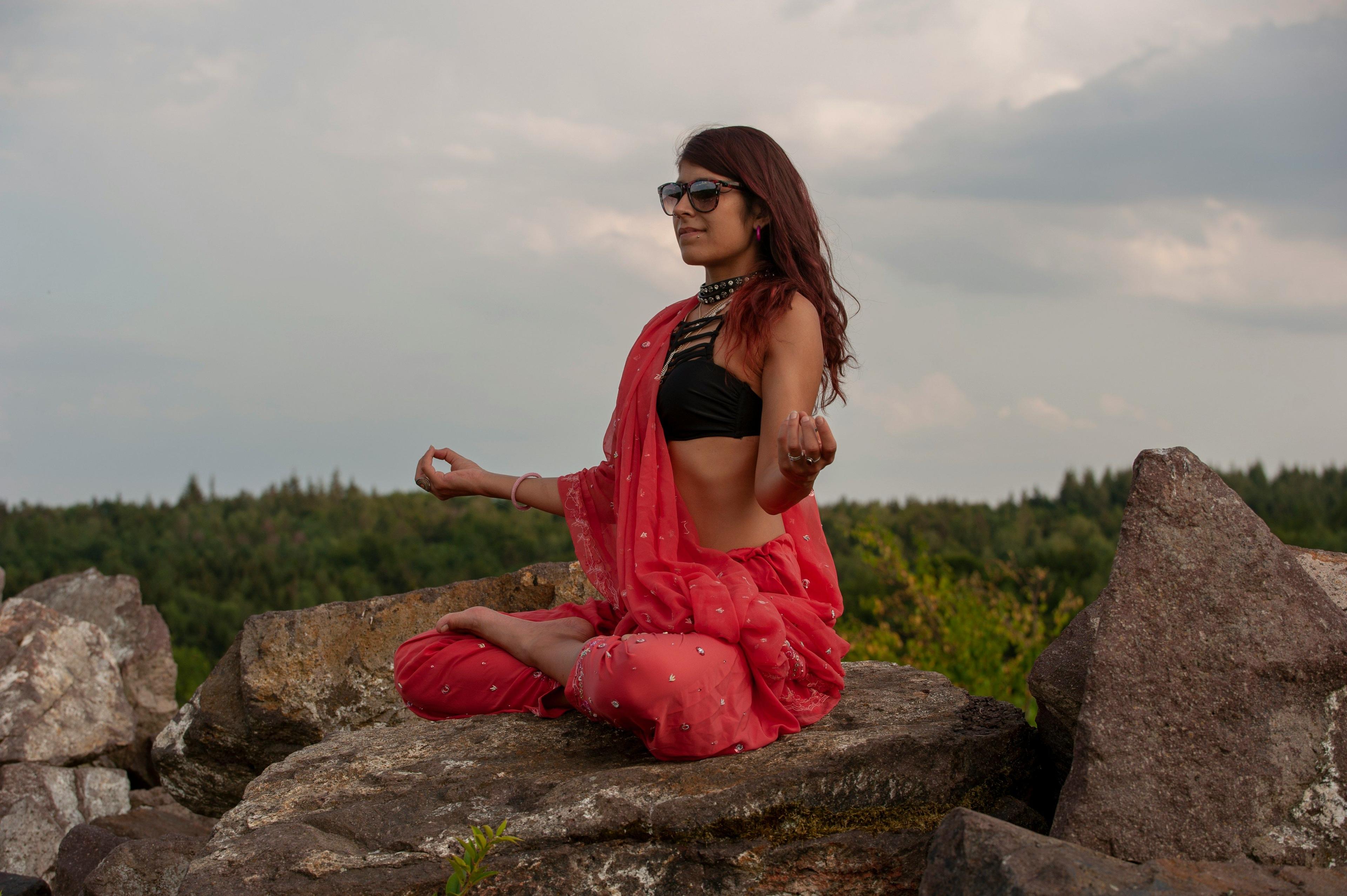 a woman sitting on top of a rock next to a forest